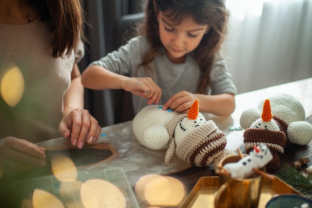 Niña linda y hermosa joven hacen muñecos de nieve de punto mamá e hija están cosiendo botones