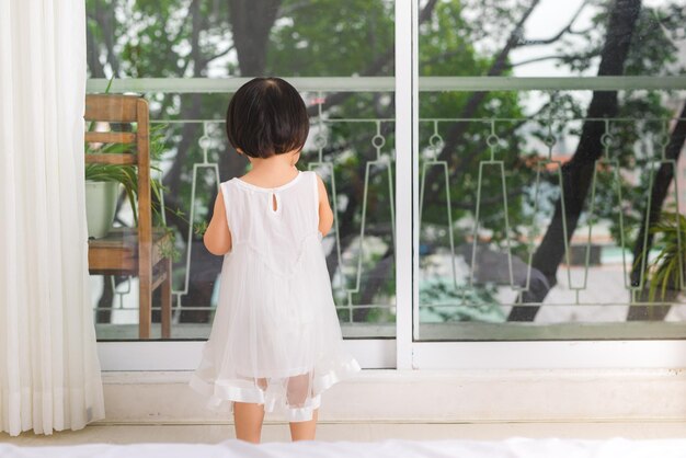 Una niña linda con un hermoso vestido está sentada cerca de la ventana en casa