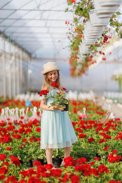 Una niña linda con un hermoso vestido en un invernadero el niño lleva un sombrero en las manos tiene una olla con una flor la niña sonríe y disfruta de la vida