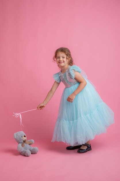 Niña linda con un hermoso vestido sosteniendo una varita mágica de hadas sobre un fondo rosa