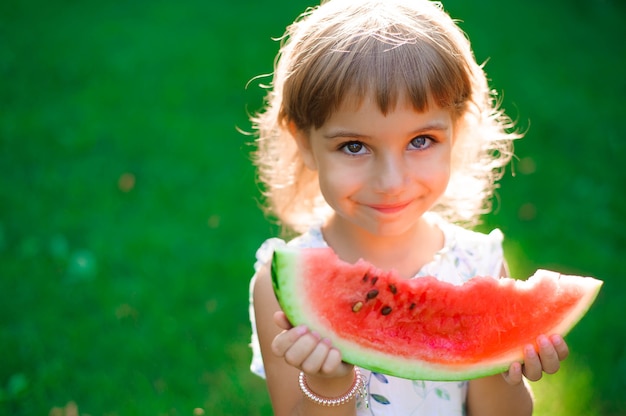 Niña linda con heterocromía de dos ojos de color comiendo sandía y disfrutando de un picnic en el parque. Naturaleza, estilo de vida