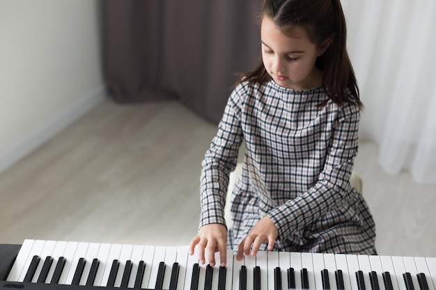 Niña linda juega en piano, sintetizador. Capacitación. Educación. Colegio. Formación estética. Aula de primaria.