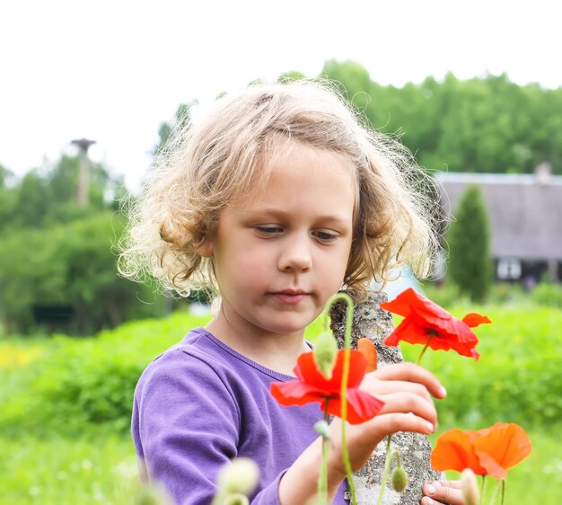 Niña linda jugando al aire libre en un prado con amapolas rojas florecientes en verano en el campo