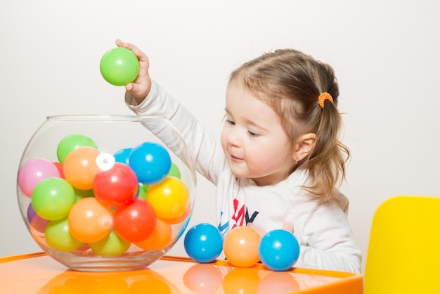 Niña linda jugando con bolas de colores en la mesa en casa