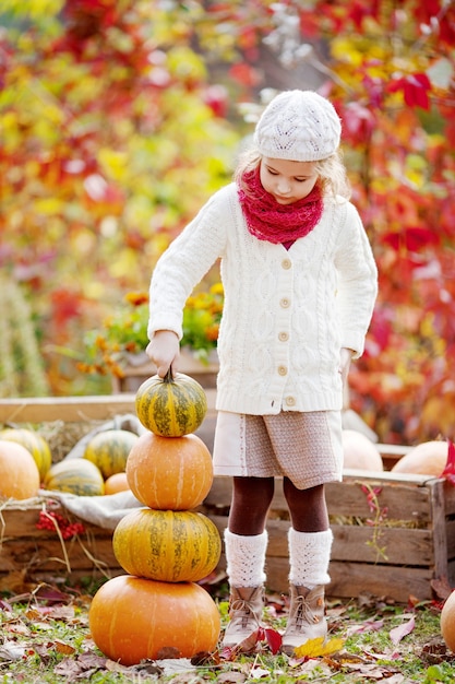 Niña linda jugando con calabazas en el parque otoño. Actividades de otoño para niños. Adorable niña construye una torre de calabazas. Diversión de Halloween y Acción de Gracias para la familia.