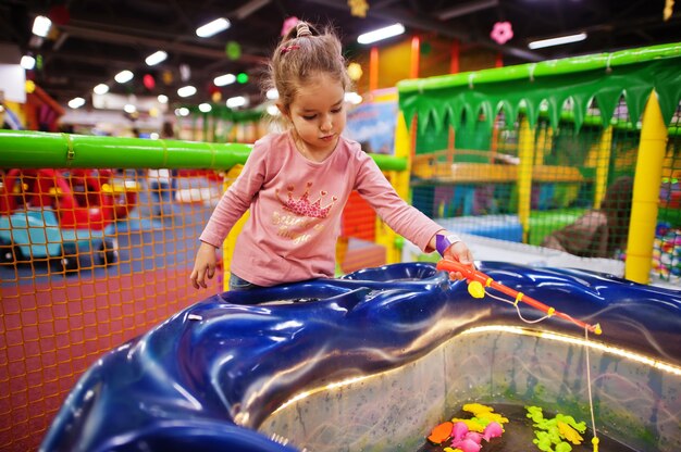 Niña linda jugando en el centro de juegos interior. Sala de juegos de jardín de infantes o preescolar. Pesca peces en la piscina.