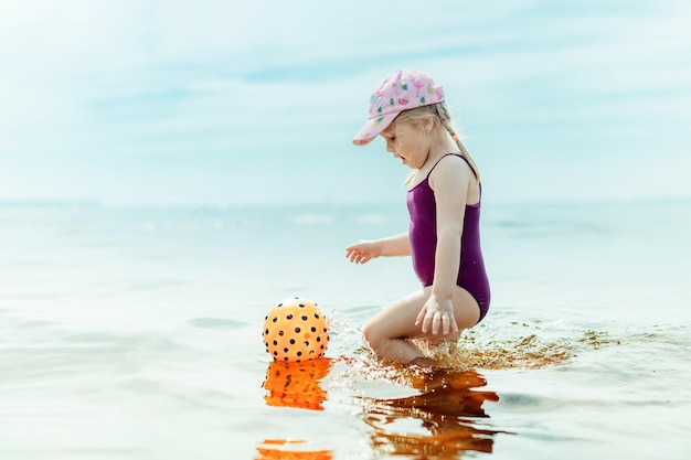 Niña linda jugando con pelota de goma en el mar