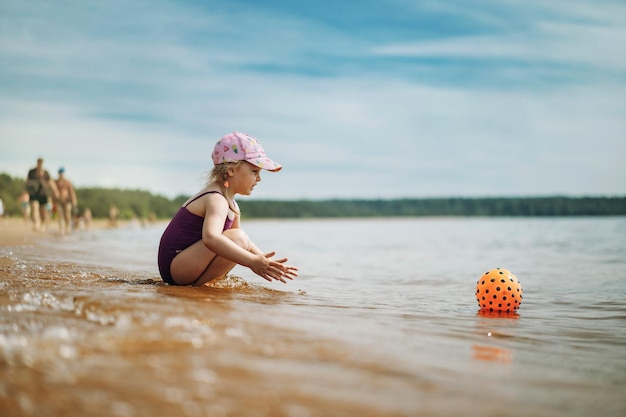 Niña linda jugando con pelota de goma en el mar