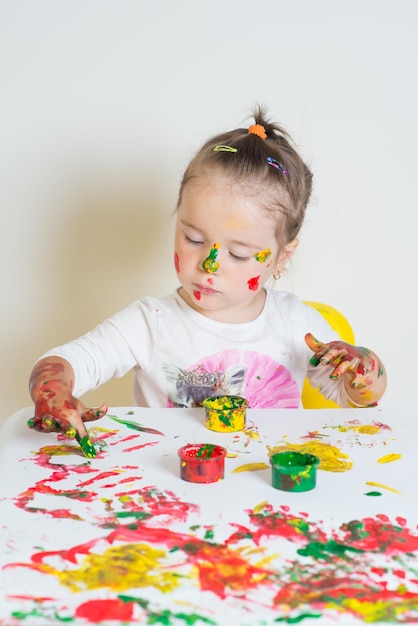 Niña linda jugando con pinturas de colores sobre un fondo blanco.