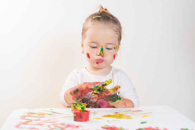 Niña linda jugando con pinturas de colores sobre un fondo blanco.