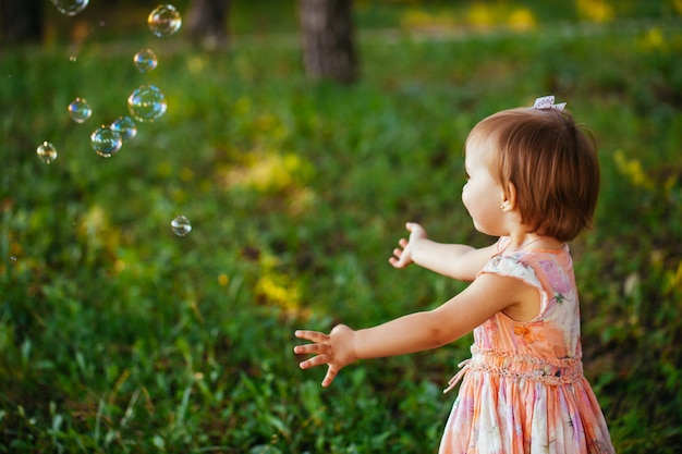 Una niña linda jugando con pompas de jabón en el parque.