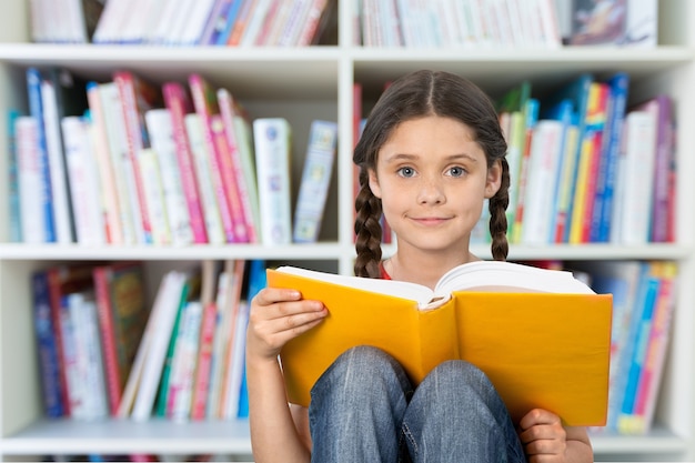 Niña linda leyendo un gran libro amarillo