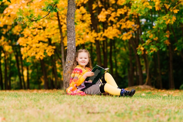 Niña linda leyendo un libro en el parque otoño