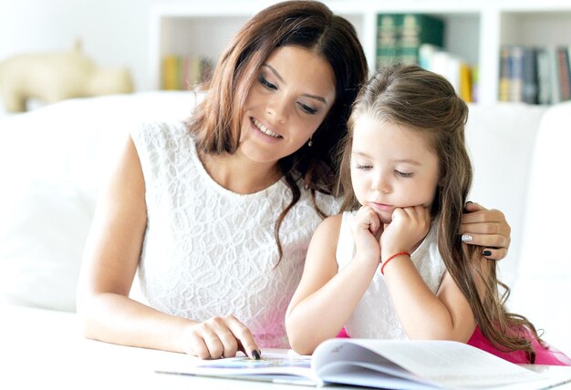 Niña linda leyendo un libro con su madre en la mesa en casa