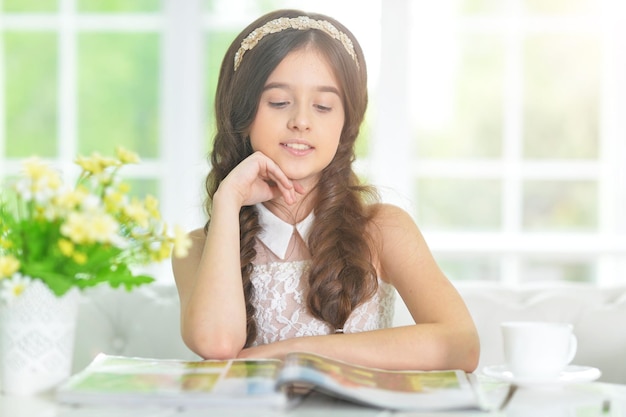 Niña linda leyendo una revista en la mesa en casa