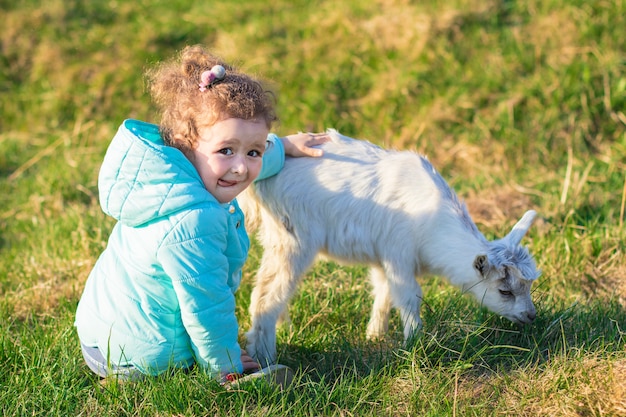 Niña linda linda, niño, niño abrazando, jugando con el cabrito o cordero en rancho, granja, patio en la hierba. Los niños aman a los animales. Concepto vegetariano, vegano. Deja de matar animales.