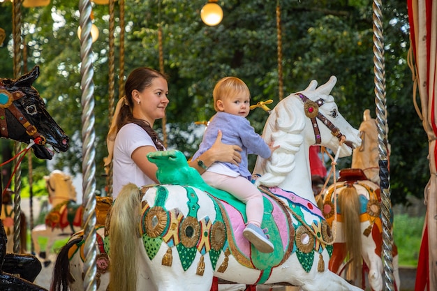 Niña linda con la madre en el caballo del antiguo carrusel retro praga república checa