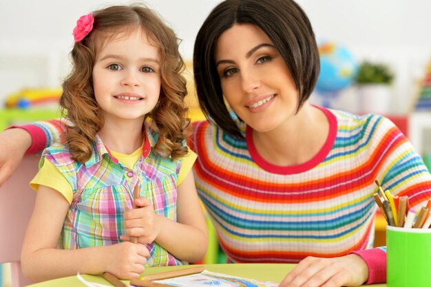 Niña linda con madre dibujando en la mesa en casa