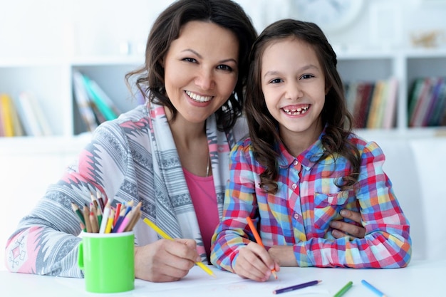 Foto niña linda con madre dibujando en la mesa en casa