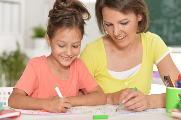 Niña linda con madre dibujando en la mesa