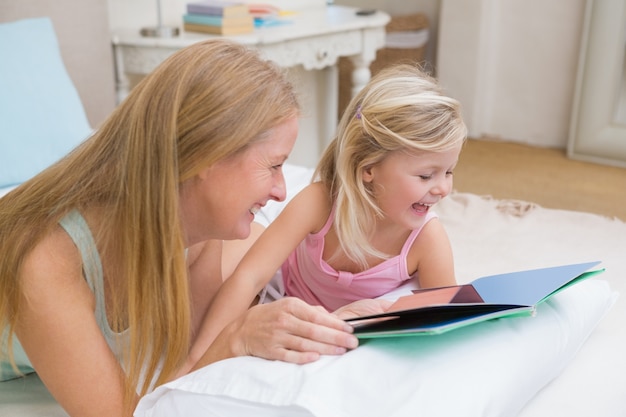 Niña linda y madre en la lectura de la cama