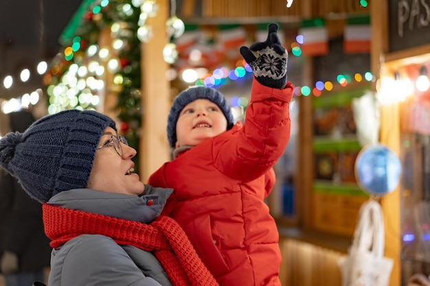 Niña linda en manos de la madre al aire libre en el mercado de Navidad