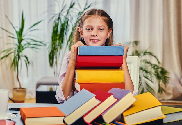 Niña linda en la mesa con muchos libros coloridos.