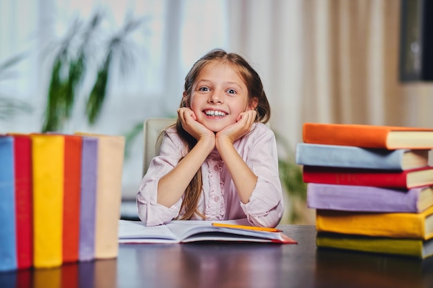 Niña linda en la mesa con muchos libros coloridos.