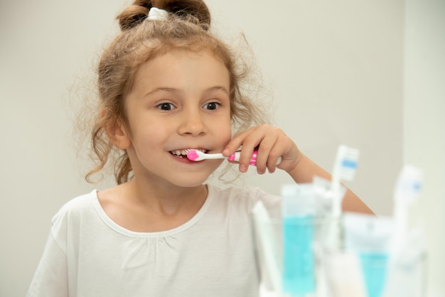 Una niña linda mira el espejo y se cepilla los dientes en el baño.