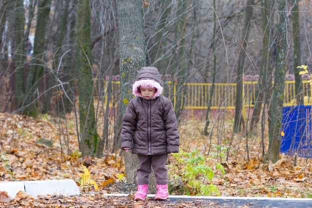 Niña linda mirando hacia abajo en el parque de otoño