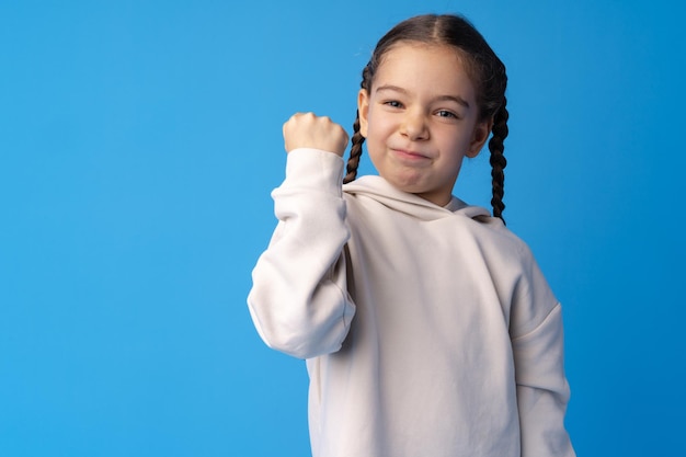 Niña linda mostrando su fuerza sobre fondo azul.