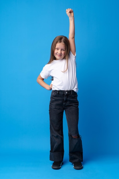 Niña linda mostrando su fuerza sobre fondo azul.