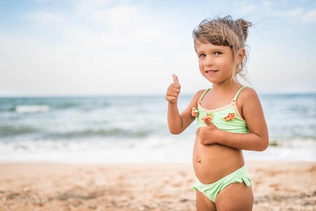 La niña linda muestra el pulgar hacia arriba mientras nada en el mar durante el fin de semana en un cálido día de verano