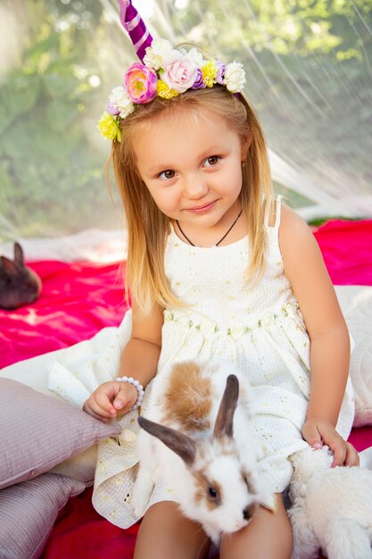 Niña linda en la naturaleza en un aro de unicornio con conejos.