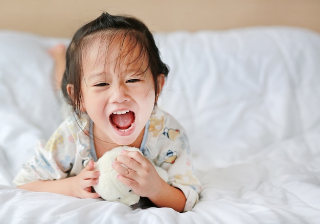 Niña linda con oso de peluche acostado en la cama