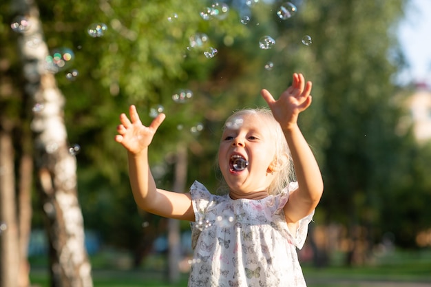 Niña linda en el parque de verano soplando burbujas y divirtiéndose.