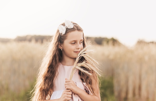 Una niña linda con el pelo largo sostiene espiguillas de trigo en el campo en verano. Verano. Concepto de cosecha