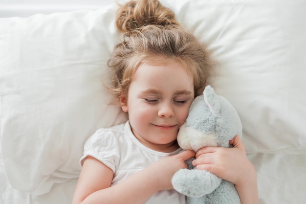 Una niña linda con el pelo rizado duerme en una cama blanca con su juguete de peluche Sueño saludable El niño está descansando