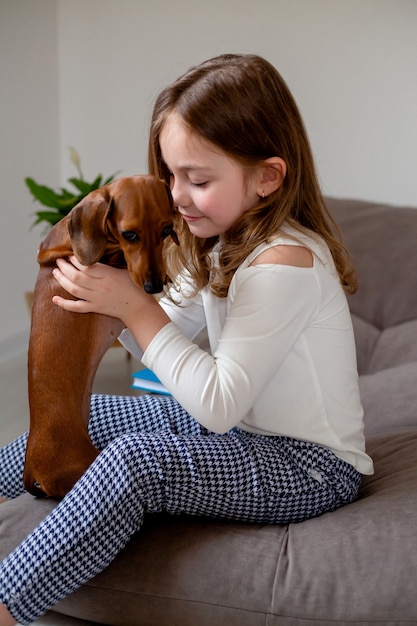 Niña linda y un perro salchicha enano están sentados en la cama nariz a nariz y se miran