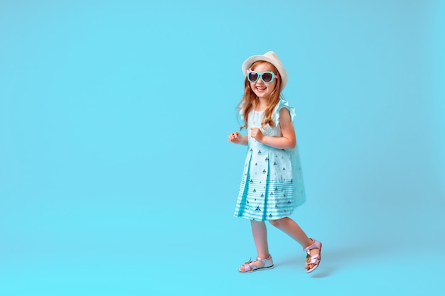 Niña linda en poses de vestido, sombrero y gafas de sol