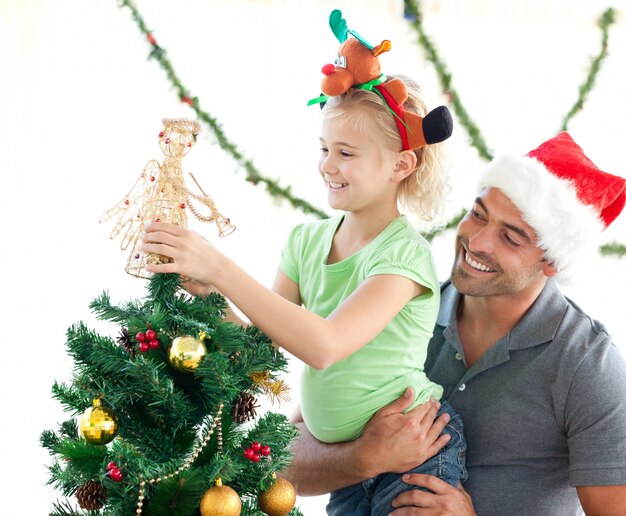 Niña linda que adorna el árbol de navidad con su padre