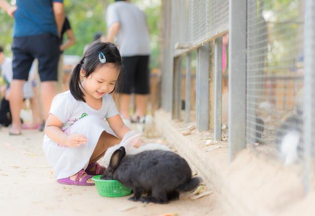 Niña linda que alimenta el conejo en la granja