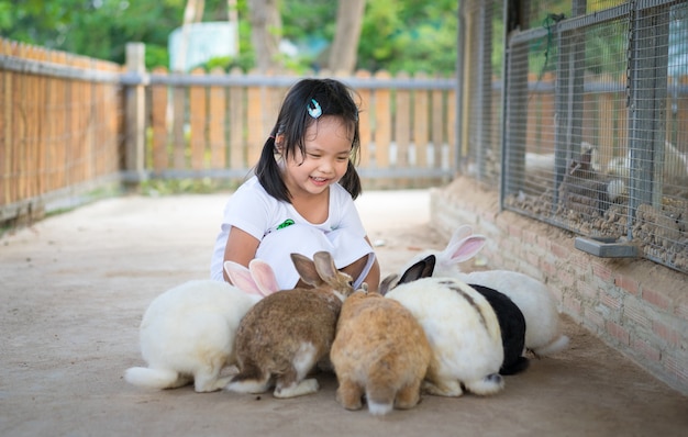 Niña linda que alimenta el conejo en la granja