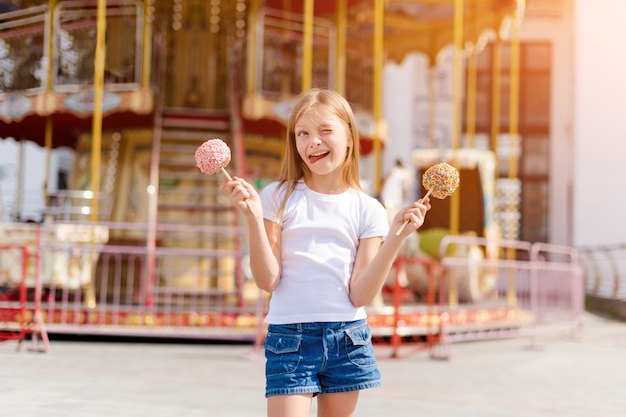 Niña linda que come la manzana de caramelo en una feria