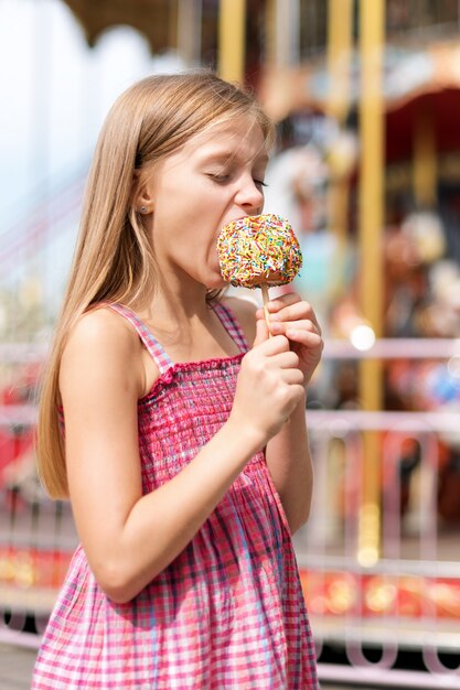 Niña linda que come la manzana de caramelo en una feria