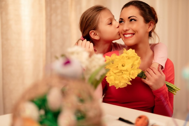 Foto niña linda que le da a su madre un ramo de narcisos amarillos y te besa.