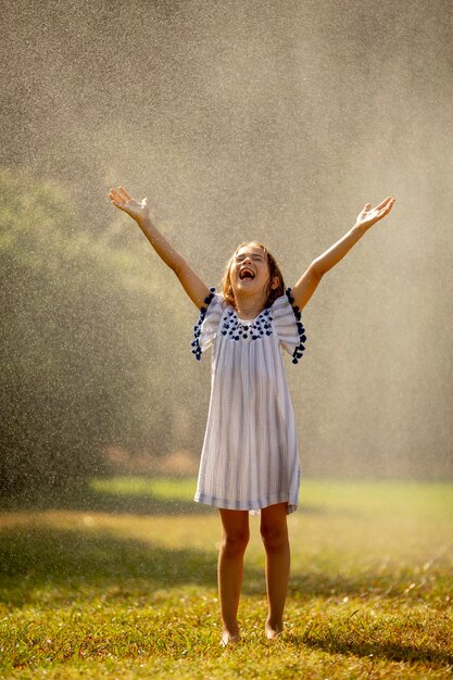 Niña linda que se divierte con agua bajo aspersión de riego