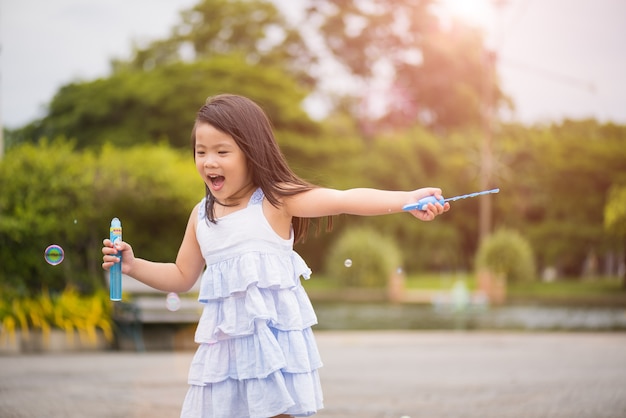 Niña linda que se divierte con soplar pompas de jabón en el parque de verano