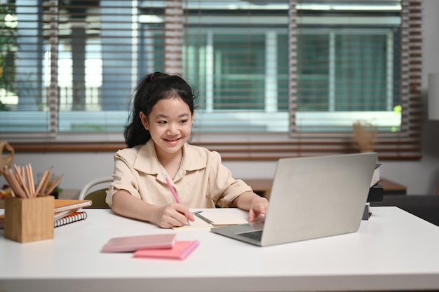 Niña linda que estudia a través del sistema de aprendizaje electrónico en línea en una computadora portátil en casa