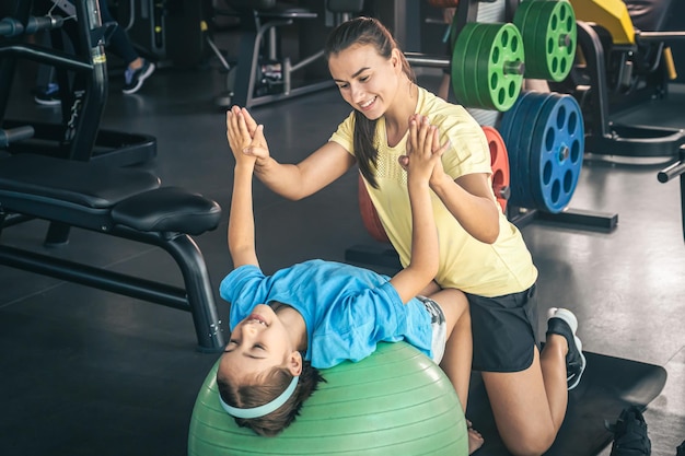 Niña linda que se extiende sobre la pelota de fitness pilates con mamá en el gimnasio